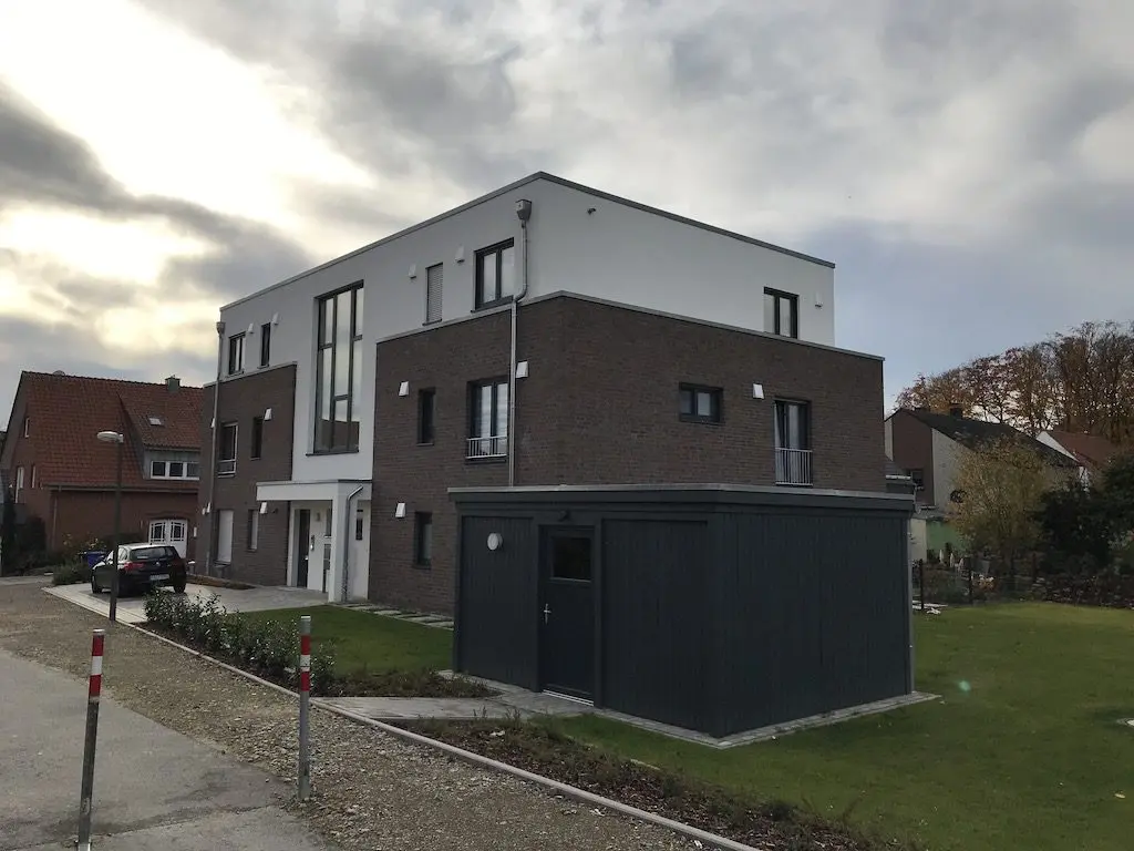 IMG_3017.jpg: Modernes Mehrfamilienhaus mit Garage und Garten unter bewölktem Himmel.