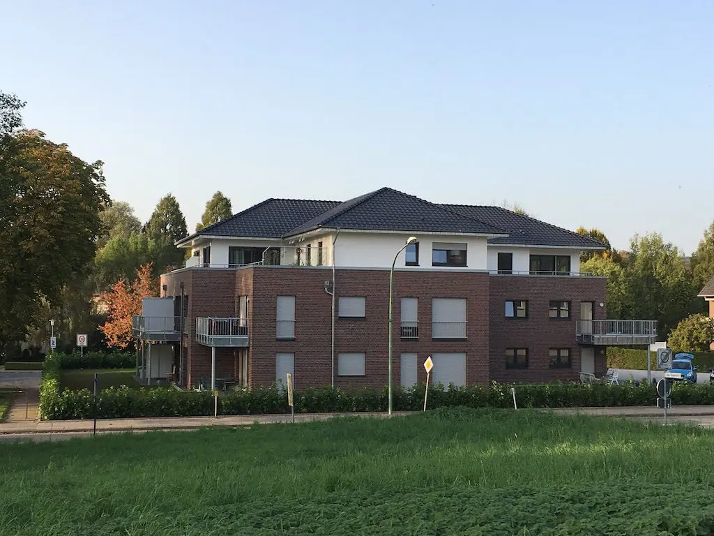 Modernes Mehrfamilienhaus mit Backsteinfassade, dunklem Dach und Balkonen, umgeben von Grün.
