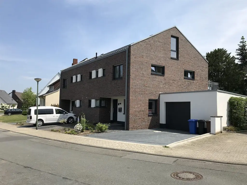 Ansicht eines modernen Reihenhauses mit Garage und geparktem Auto an einer Wohnstraße.
