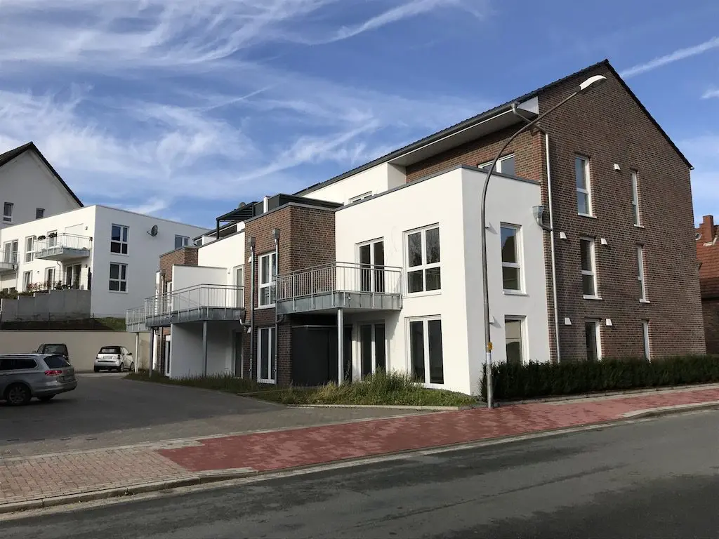 Ansicht eines modernen Mehrfamilienhauses mit Balkonen und Parkplätzen unter blauem Himmel.