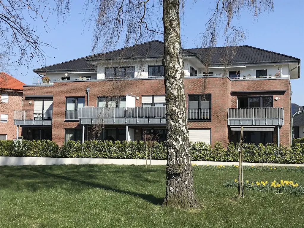 Mehrfamilienhaus mit Backsteinfassade, Balkonen und gepflegtem Garten im Vordergrund.