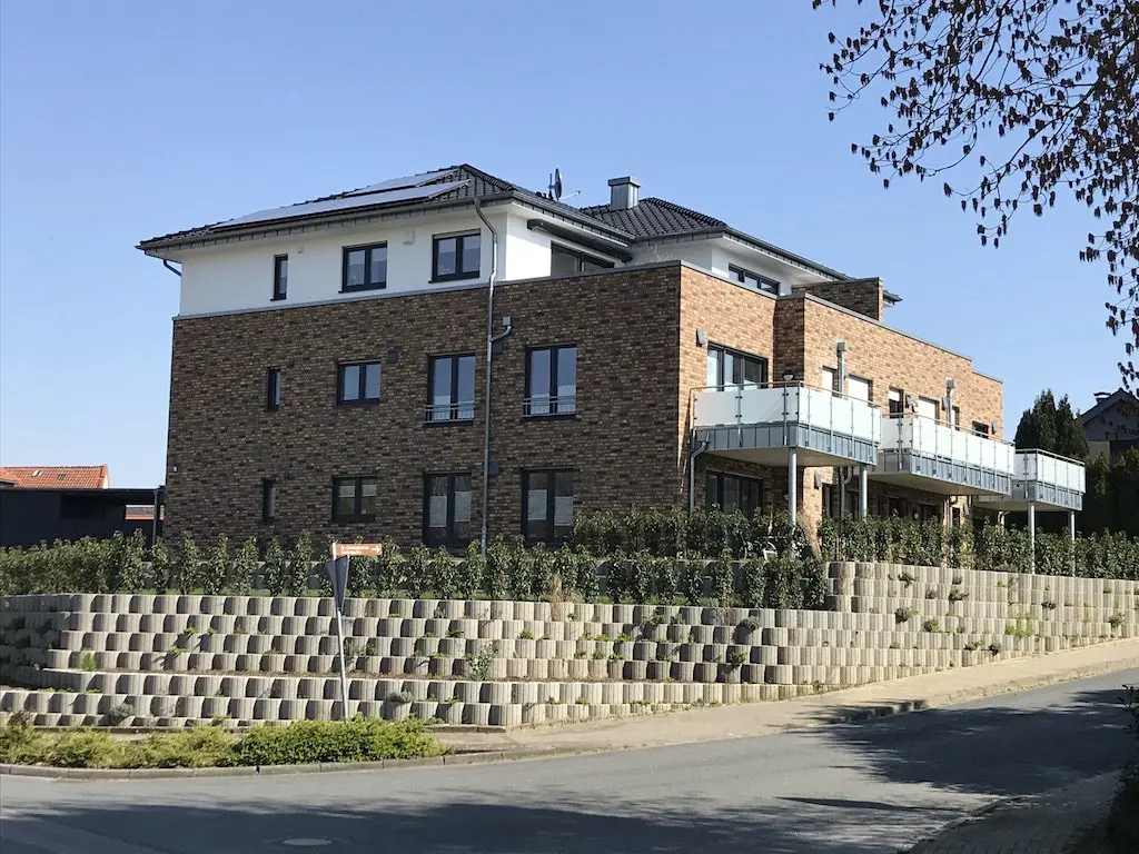 Mehrgeschossiges Wohngebäude mit Balkonen und Ziegelmauerwerk vor blauem Himmel.