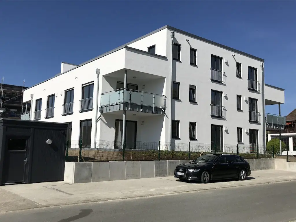 Modernes, weißes Mehrfamilienhaus mit Balkonen und geparktem Auto im Freien.