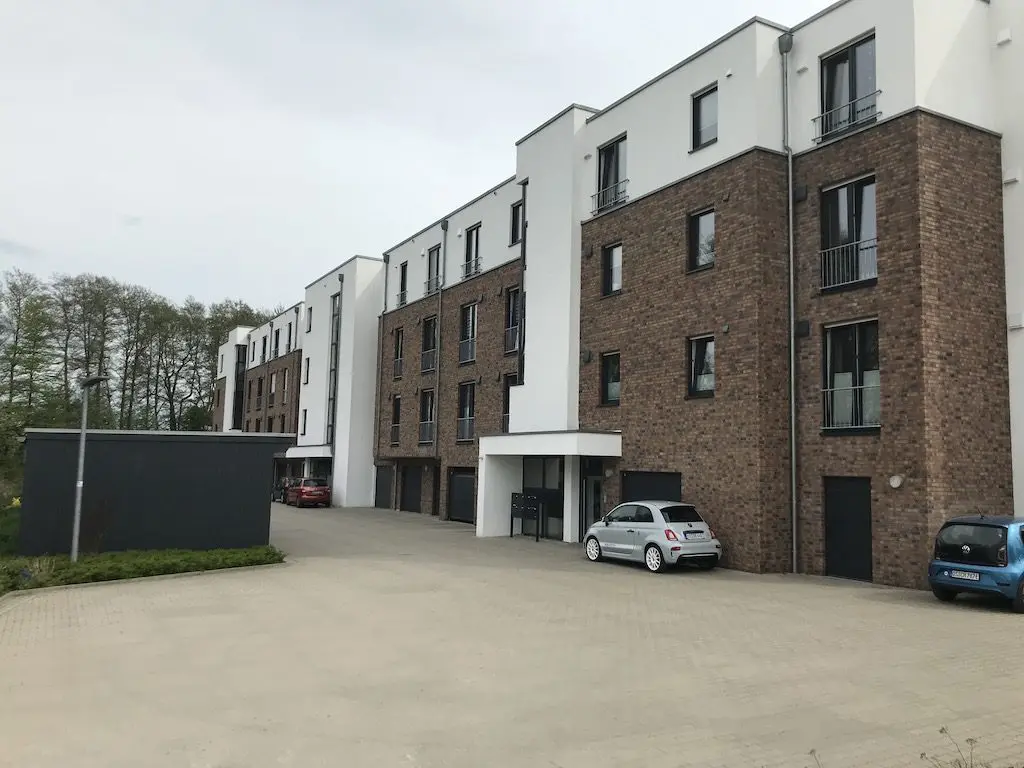 Ansicht eines modernen Mehrfamilienhauses mit Backsteinfassade und geparkten Autos.