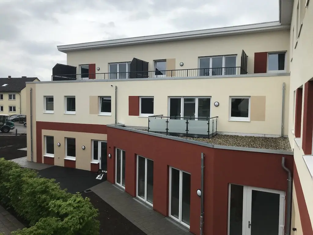 Mehrgeschossiges Gebäude mit Balkonen und Farbgestaltung in Rot- und Beigetönen, aufgenommen mit IMG_8739.jpg