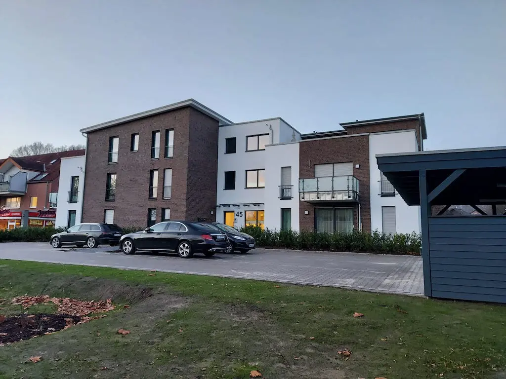Mehrgeschossiges Wohngebäude mit geparkten Autos und Carport am Abend.