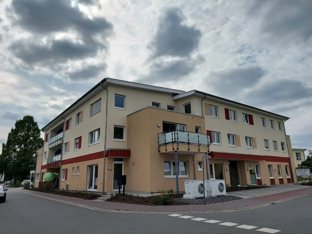 Ansicht der Wohnanlage mit Tagespflege, mehrstöckiges Gebäude mit Balkonen unter bewölktem Himmel.
