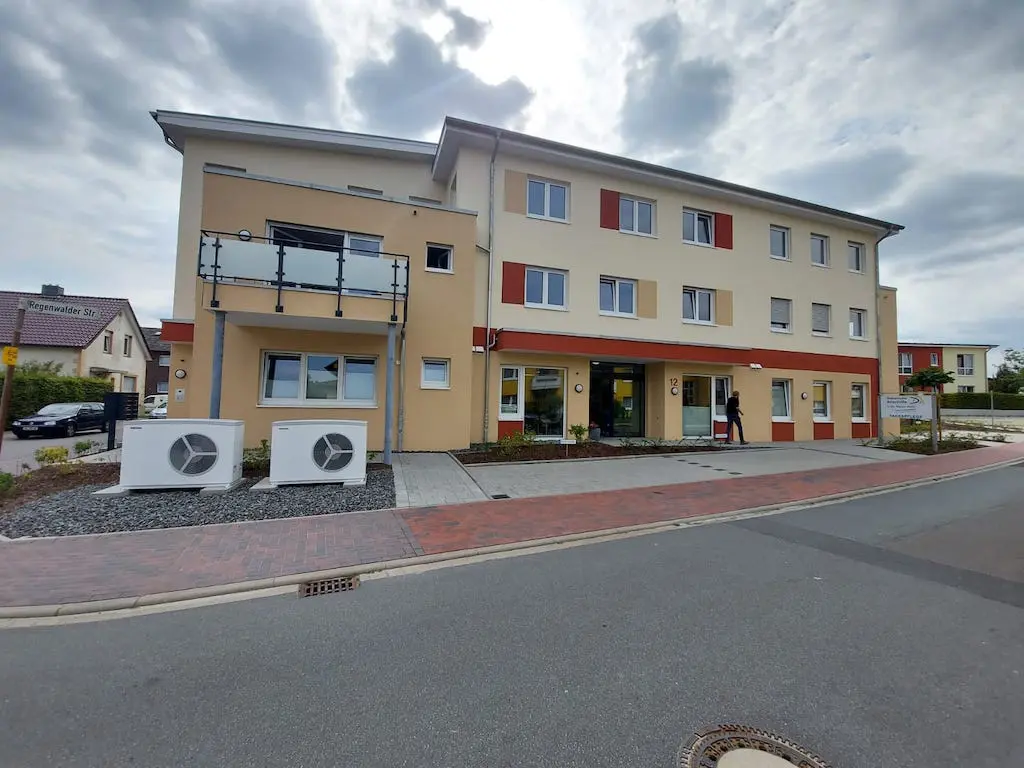 Ansicht der Wohnanlage mit Tagespflege, ein mehrstöckiges Gebäude mit Balkon und mehreren Fenstern.