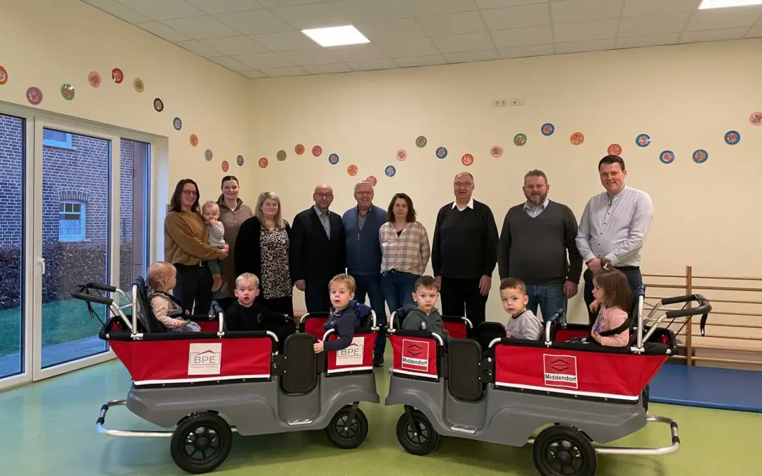 Kindergarten: Gruppe mit Kinderwagen und Kindern vor Erwachsenen im Innenraum.