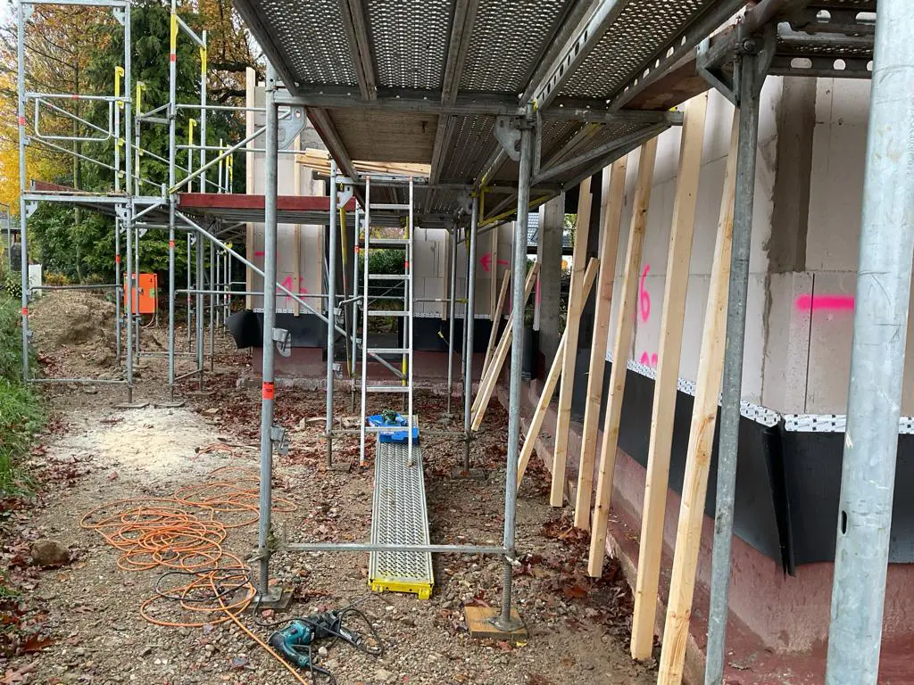 Baustelle mit Gerüst, unfertiger Fassade und Werkzeugen im Außenbereich. Bauarbeiten sind im Gange.