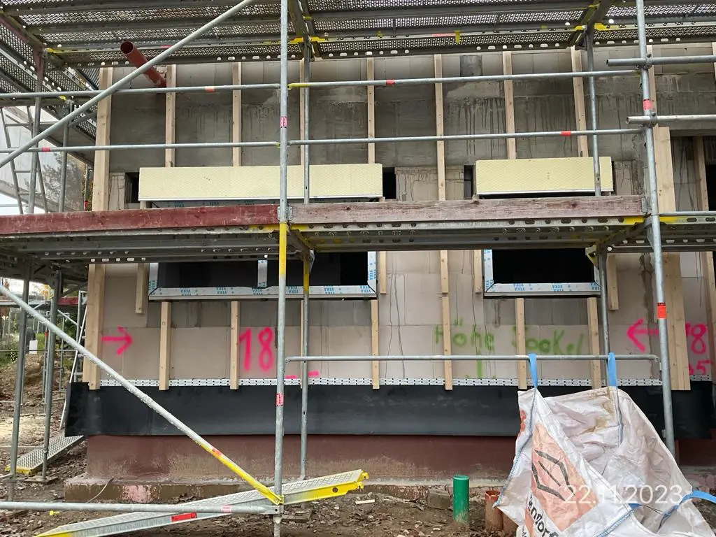 Hausbau: Fassade mit Gerüst und Dämmung, Fensteröffnungen sichtbar.