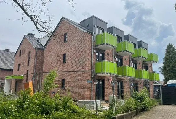 Neues Backsteingebäude mit modernen grünen Balkonen unter bewölktem Himmel.