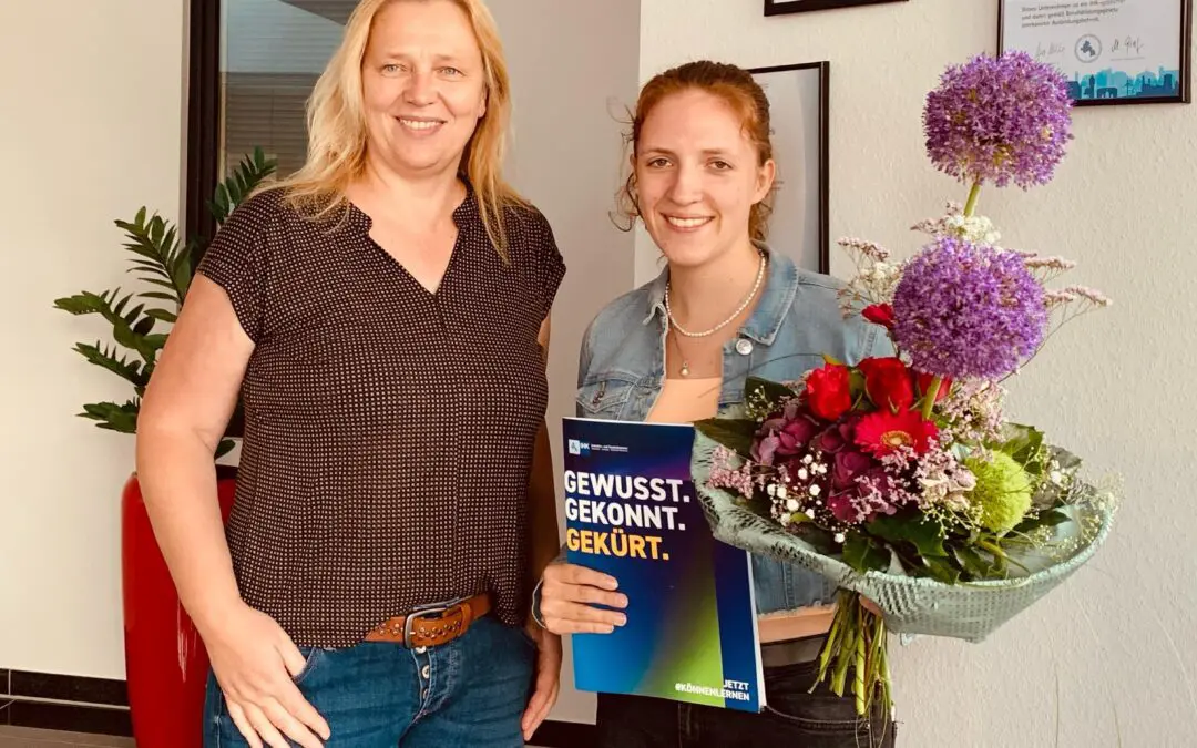 Zwei Frauen, eine hält Blumen und eine Broschüre mit der Aufschrift "Gewusst. Gekonnt. Gekürt."